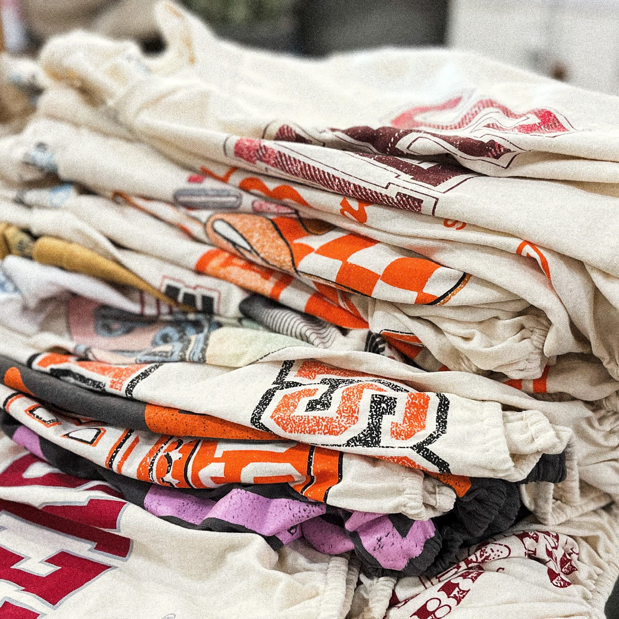 Variety of OU Sooners t-shirts, OSU Cowboys t-shirts, band t-shirts folded and stacked on top of each other from Lush Fashion Lounge boutique in Oklahoma City 